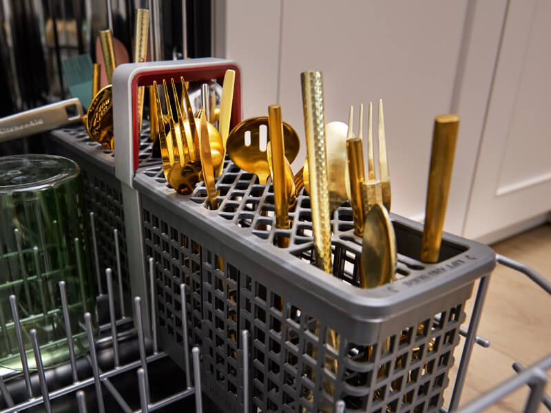 Gold colored utensils in a dishwasher utensils bin