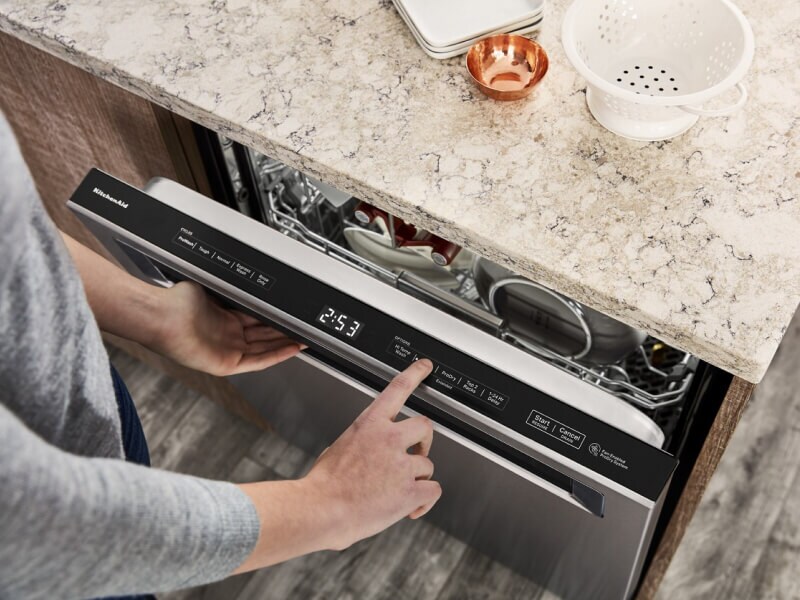 A hand selecting settings on a KitchenAid® dishwasher