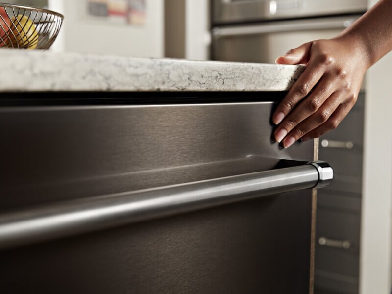 Hand touching the exterior of a sleek dishwasher