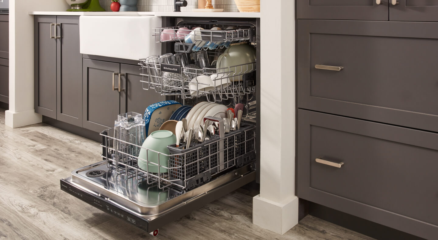 An opened and fully loaded dishwasher inside a kitchen