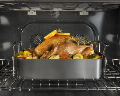 A turkey in a roasting pan on the top rack inside an oven range