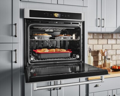 A single wall oven with the oven door open, showing items cooking on both racks