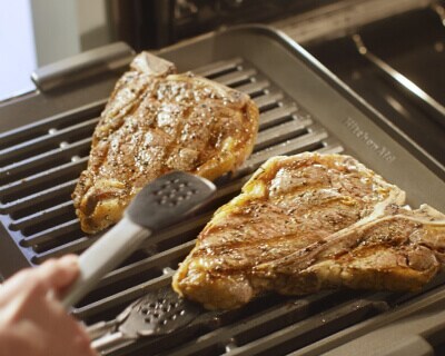 A hand flipping chicken on a grill pan with silver tongs