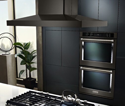 Island mount hood over a cooktop in an island countertop in front of a double wall oven