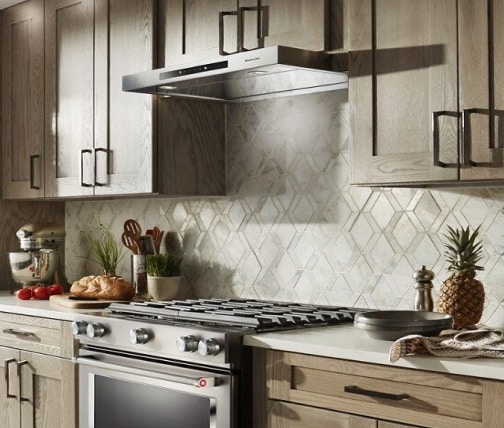Low profile under cabinet hood between light wood cabinets over a slide-in range