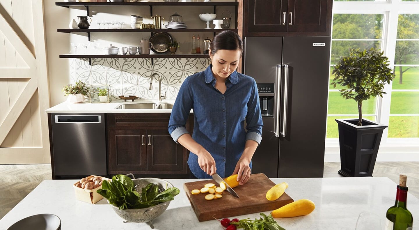 A person cutting vegetables in a kitchen with black stainless steel appliances A person cutting vegetables in a kitchen with black stainless steel appliances