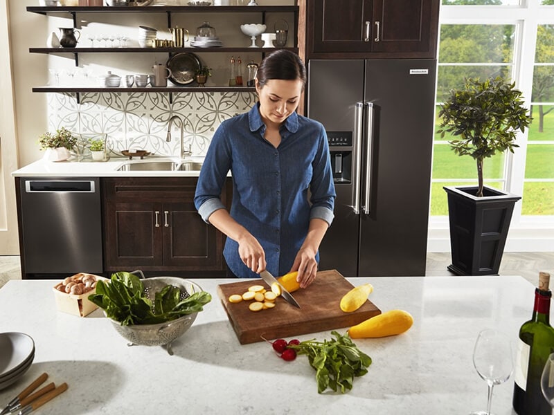 A person cutting vegetables in a kitchen with black stainless steel appliances A person cutting vegetables in a kitchen with black stainless steel appliances