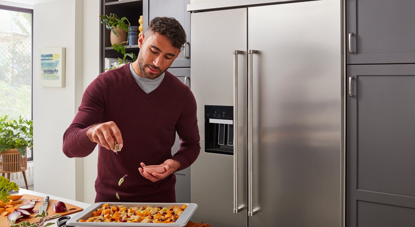 Person seasoning food in front of a stainless steel side-by-side refrigerator Person seasoning food in front of a stainless steel side-by-side refrigerator
