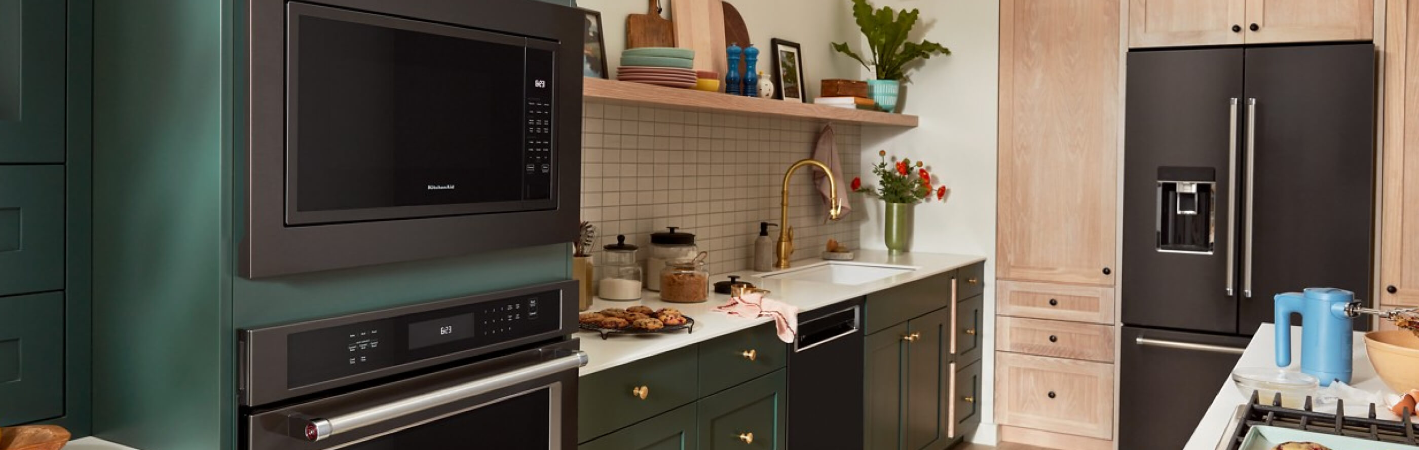 Suite of black stainless steel KitchenAid® appliances in green and natural brown cabinetry