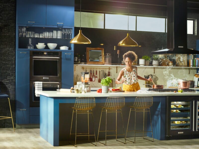 Person cooking in a kitchen with deep blue cabinets and black stainless steel KitchenAid® appliances Person cooking in a kitchen with deep blue cabinets and black stainless steel KitchenAid® appliances