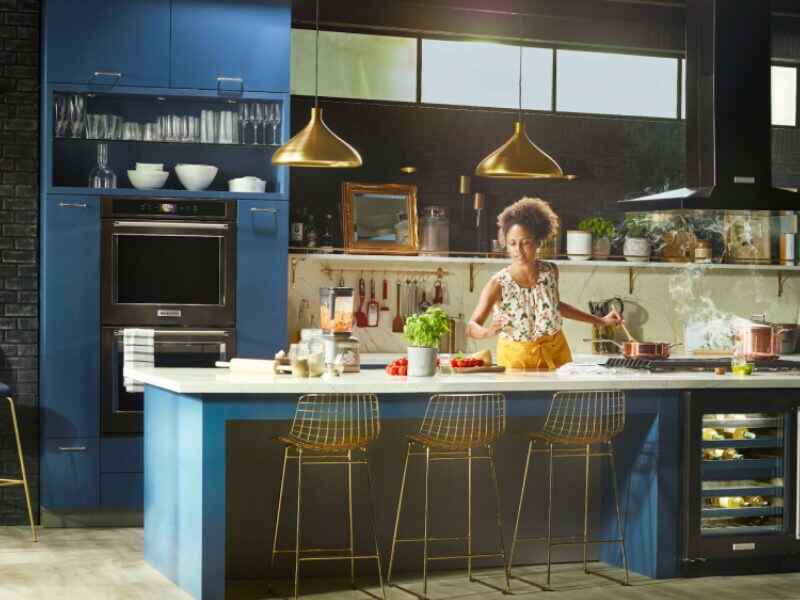 Person cooking in a kitchen with deep blue cabinets and black stainless steel KitchenAid® appliances Person cooking in a kitchen with deep blue cabinets and black stainless steel KitchenAid® appliances