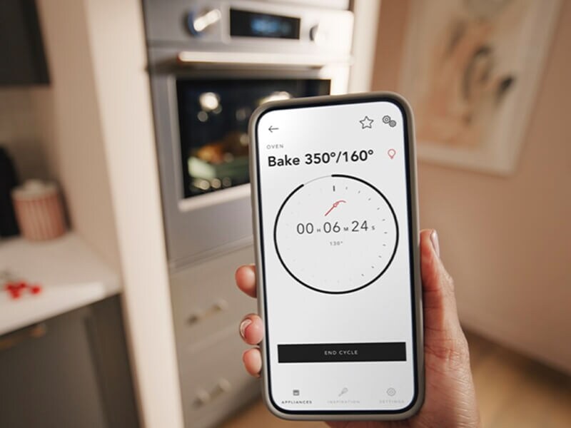 A person holding a phone in front of a KitchenAid® wall oven
