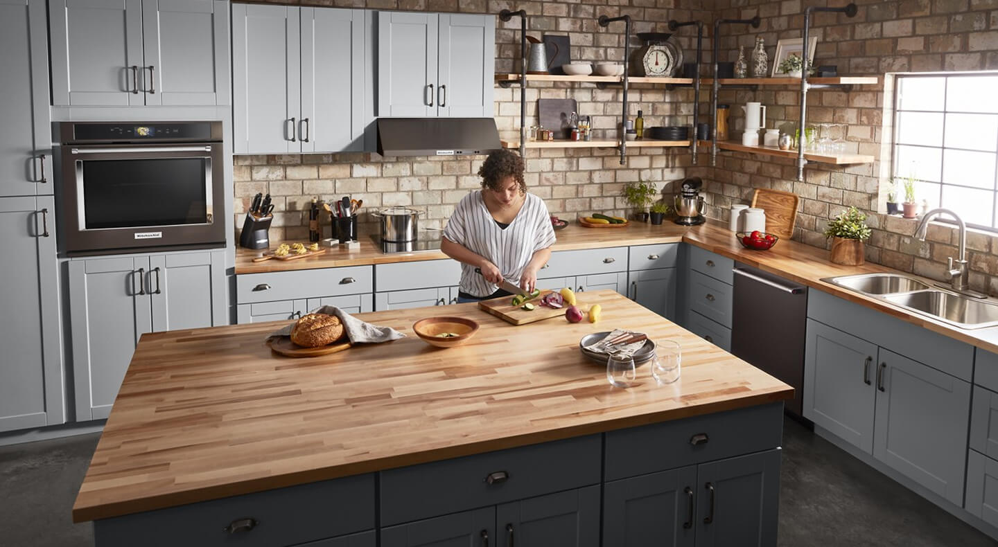 A person preparing food at a large island with a butcher block top