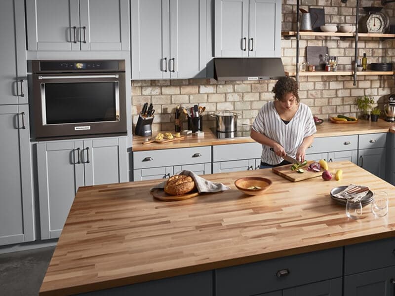 A person preparing food at a large island with a butcher block top