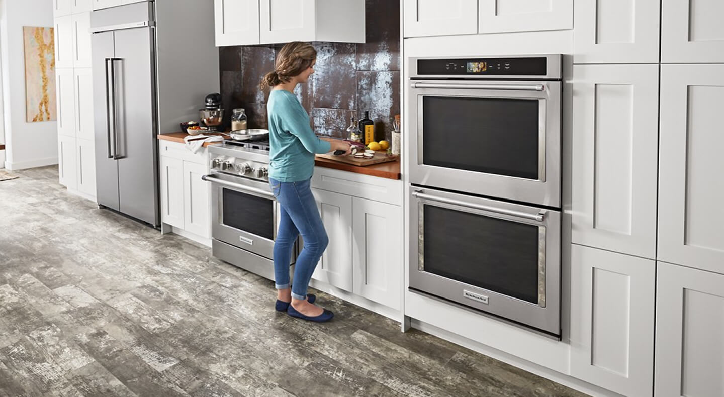 A person standing at a counter next to a wall oven preparing food