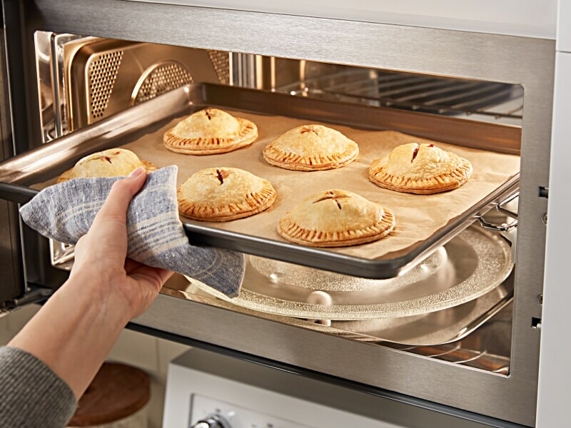 A person removing a sheet pan of baked pastries from a KitchenAid® microwave