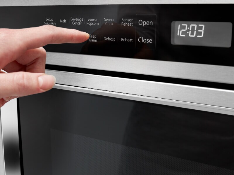 A person programming a setting on a KitchenAid® microwave