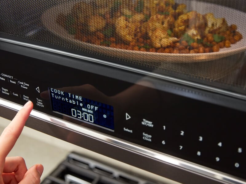 A person programming a setting on a KitchenAid® microwave