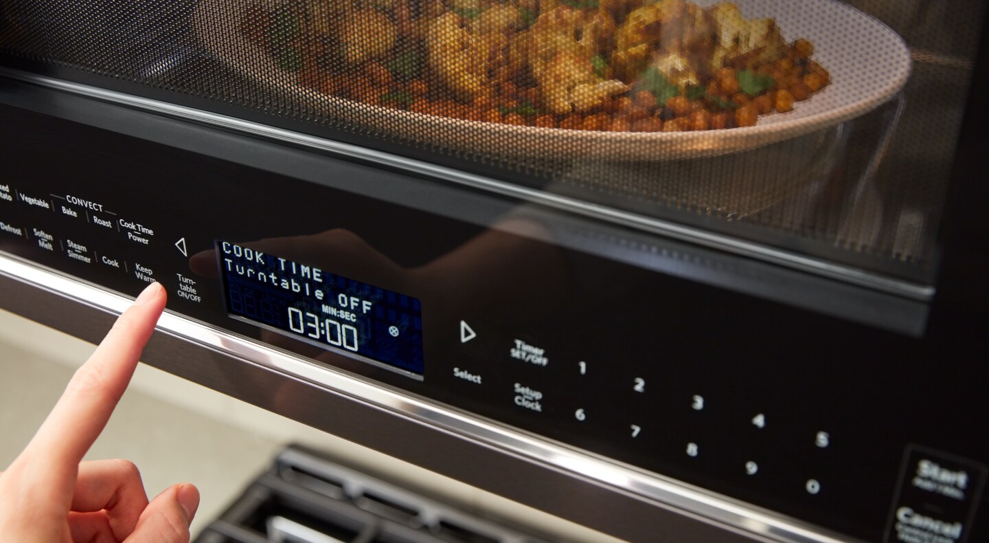 A person programming a setting on a KitchenAid® microwave. A person programming a setting on a KitchenAid® microwave.