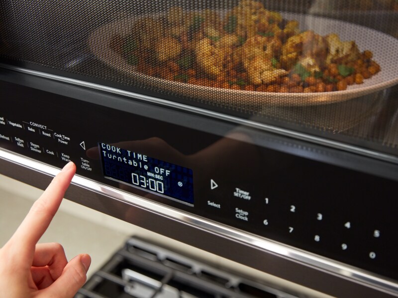 A person programming a setting on a KitchenAid® microwave. A person programming a setting on a KitchenAid® microwave.