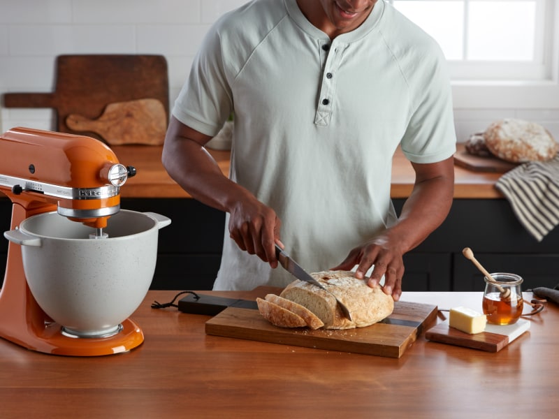 Person slicing bread next to orange stand mixer
