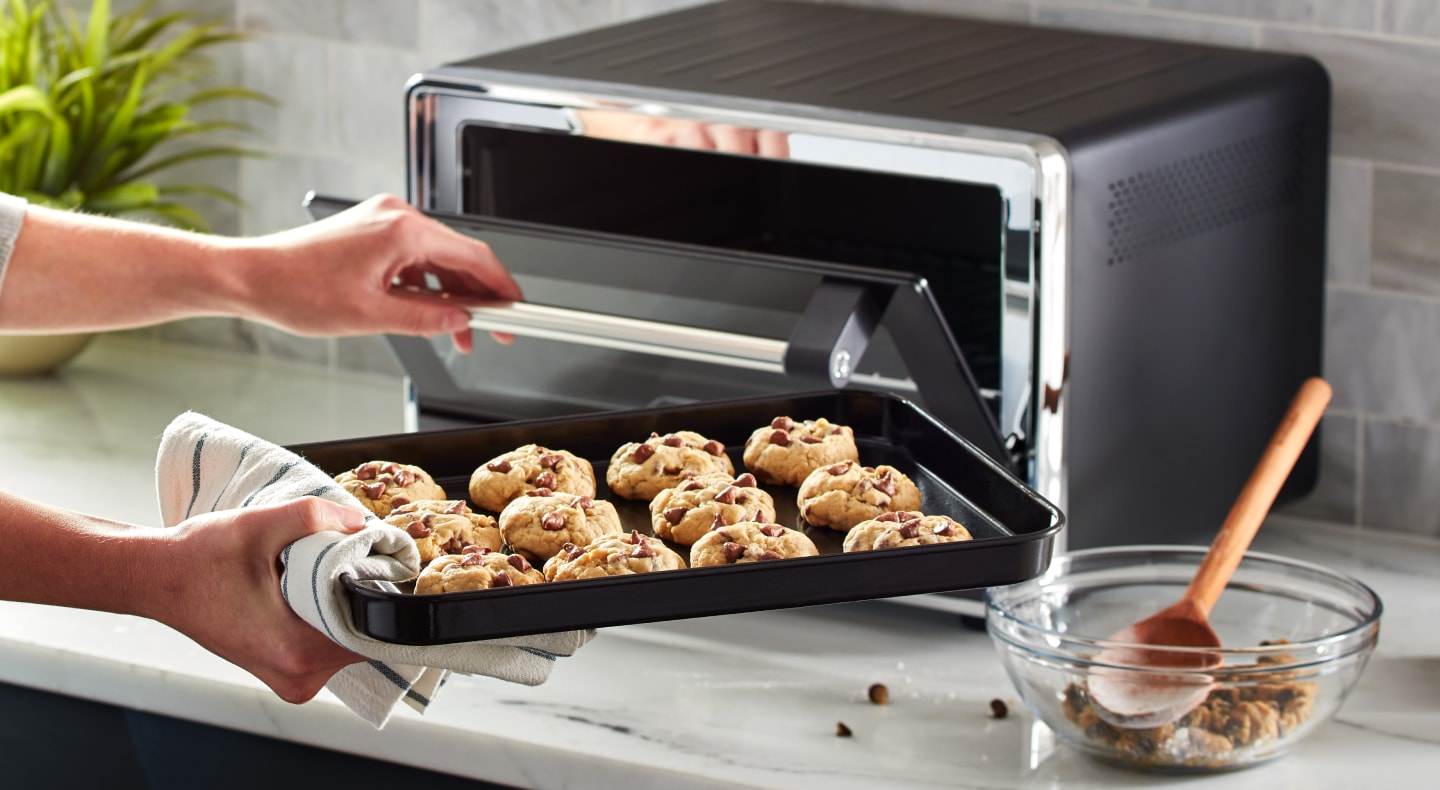 Person placing a tray of cookies into a KitchenAid® countertop oven Person placing a tray of cookies into a KitchenAid® countertop oven
