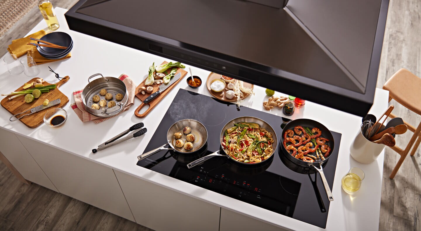 Overhead view of KitchenAid® range hood and pans with food on black cooktop
