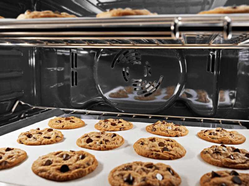 The inside of an oven with chocolate chip cookies baking on both racks