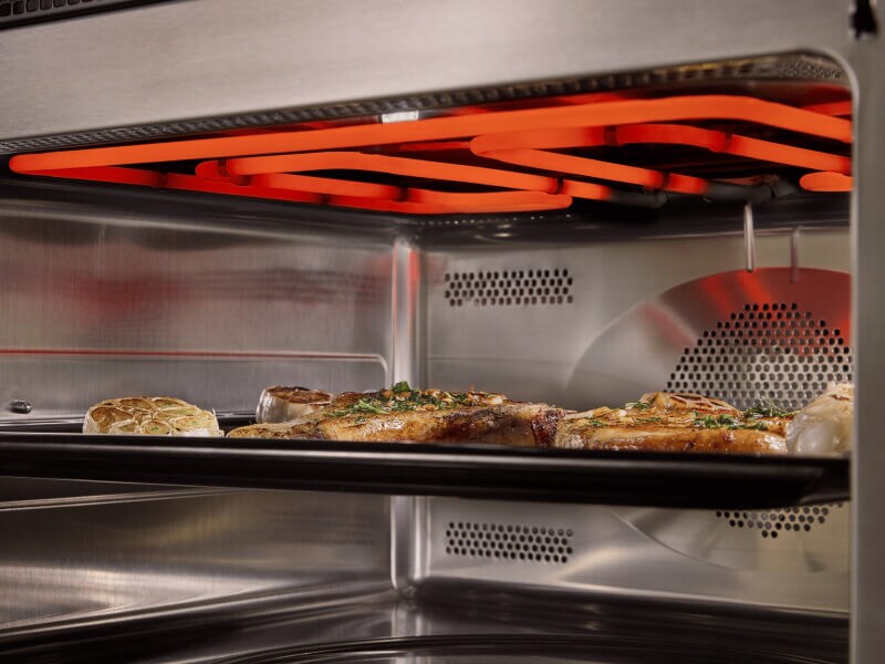 Inside of an oven with the broiler turned on and food cooking on one rack