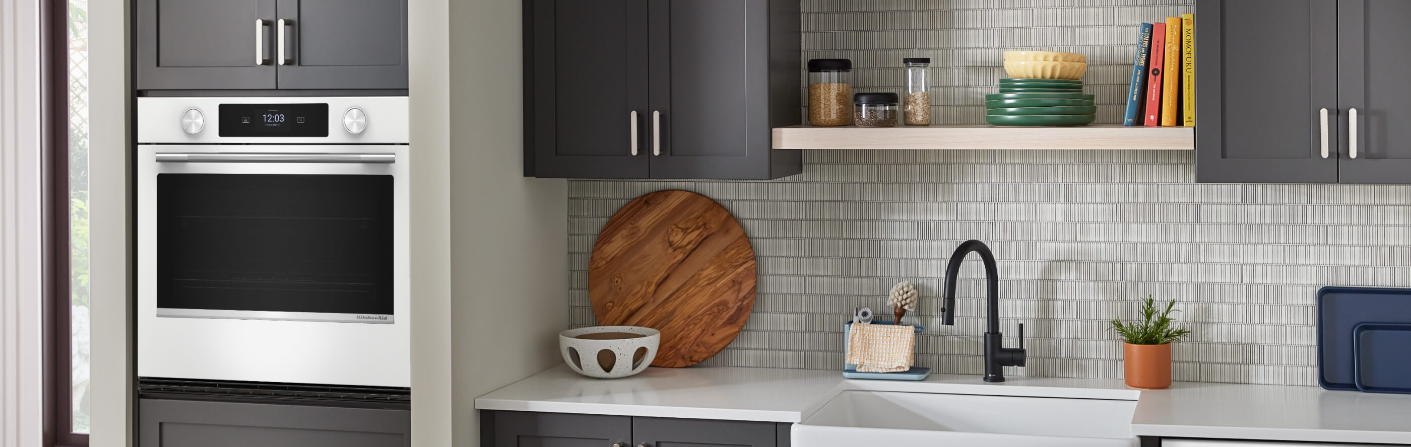 The interior of a kitchen with gray cabinetry, white countertops and a single wall oven
