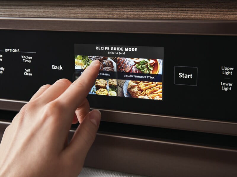 A finger pushing an assisted cooking mode on a wall oven