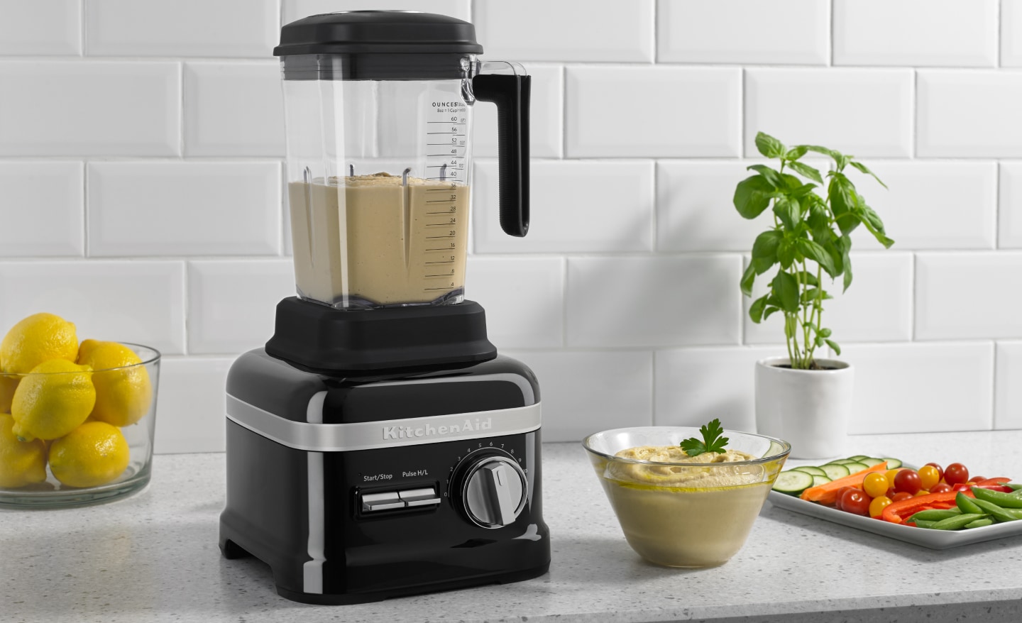 A KitchenAid® blender with hummus on a modern kitchen counter next to fresh vegetables. A KitchenAid® blender with hummus on a modern kitchen counter next to fresh vegetables.