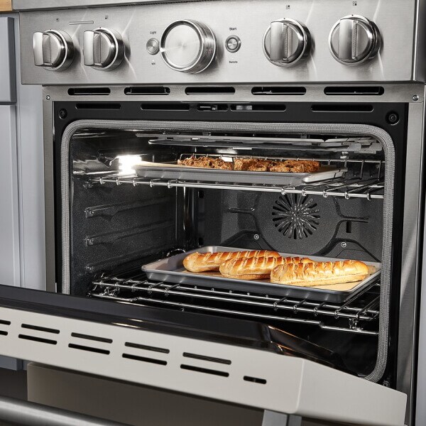 Two pans with roasting food on them in an open oven