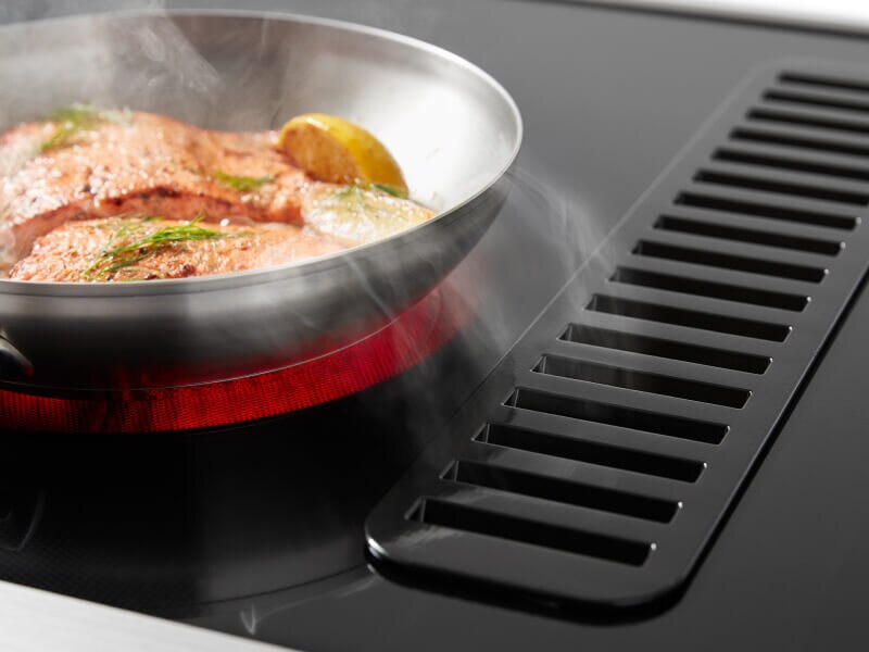 Salmon cooking on a downdraft electric range with a lit up red element Salmon cooking on a downdraft electric range with a lit up red element