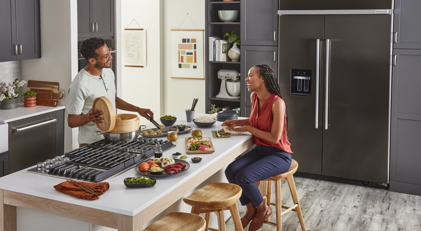 A man cooking for a woman on a downdraft gas cooktop set into a kitchen island A man cooking for a woman on a downdraft gas cooktop set into a kitchen island