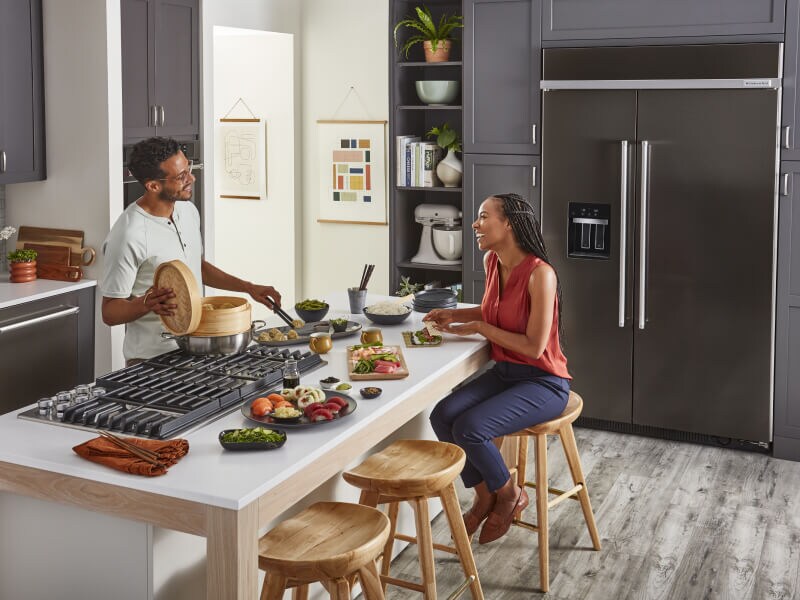 A man cooking for a woman on a downdraft gas cooktop set into a kitchen island A man cooking for a woman on a downdraft gas cooktop set into a kitchen island