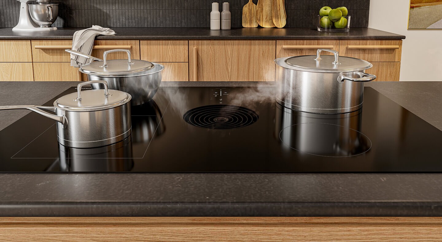An induction downdraft cooktop with steam from three stainless steel pots being pulled down the downdraft vent