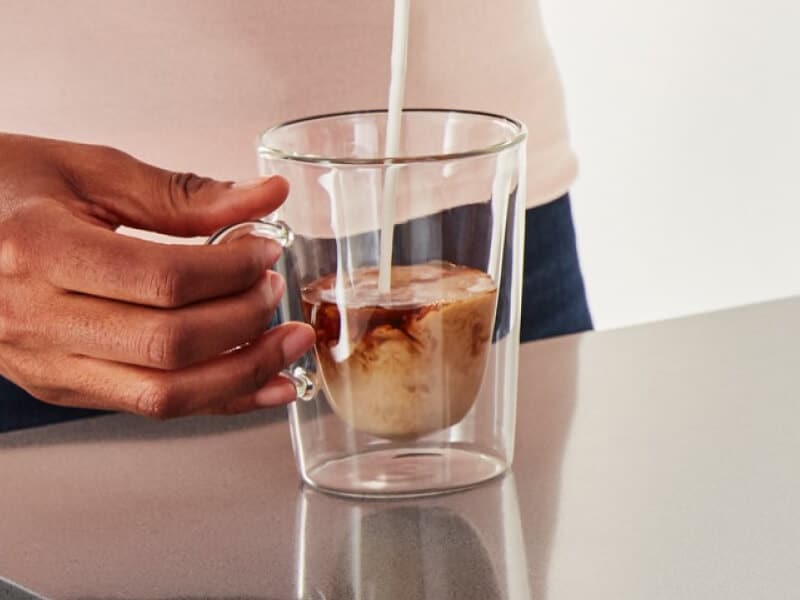Close-up of person pouring milk into espresso cup