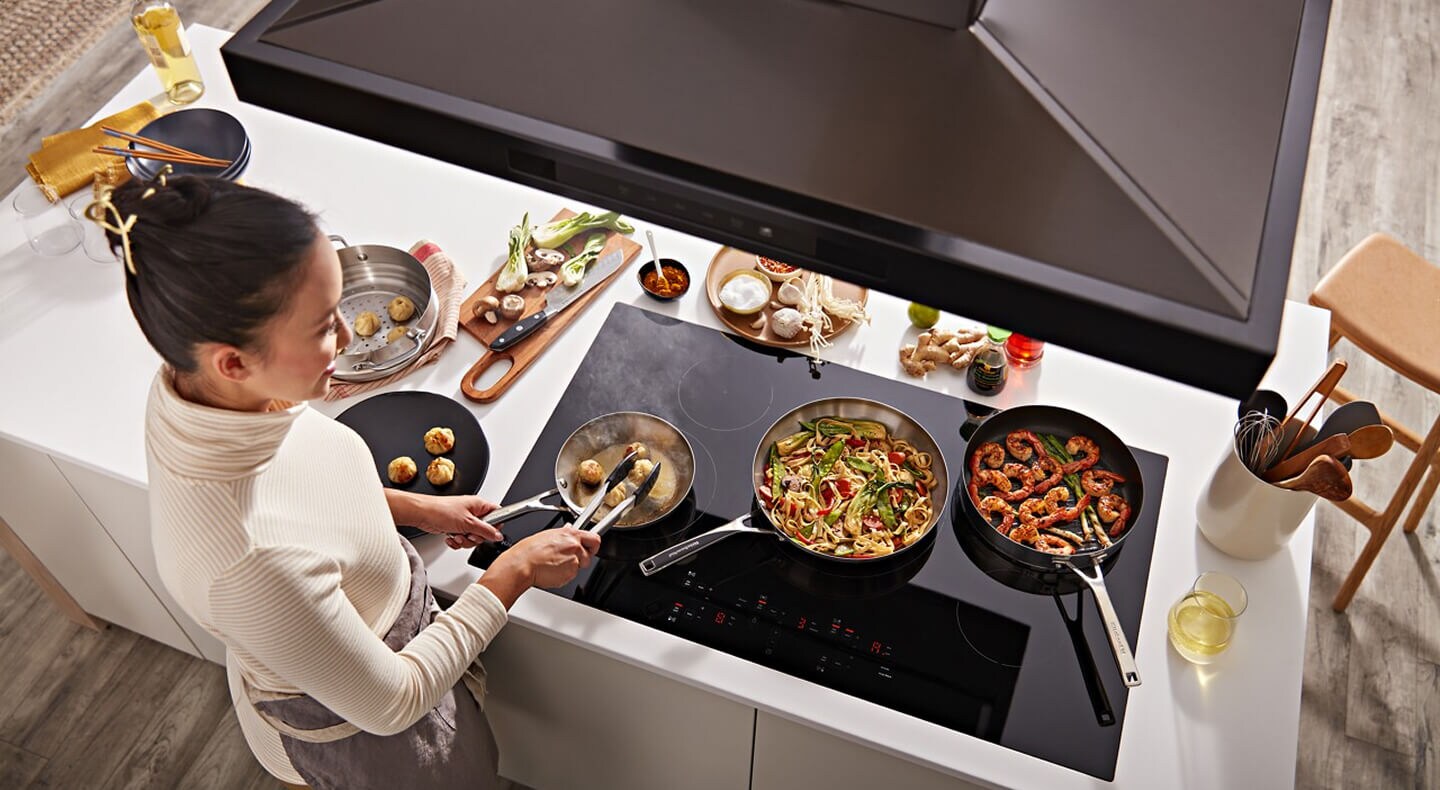 Person removing food with tongs from a pan on an induction cooktop 