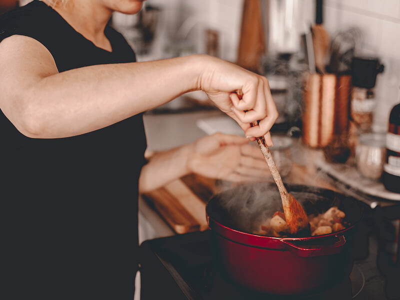 A person stirring a large Dutch oven on a stovetop