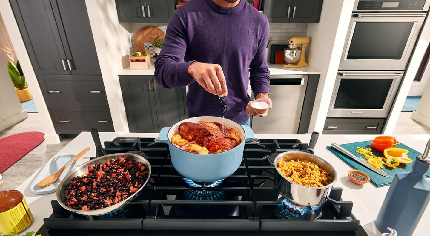 A person sprinkling seasonings over a meal simmering in a Dutch oven