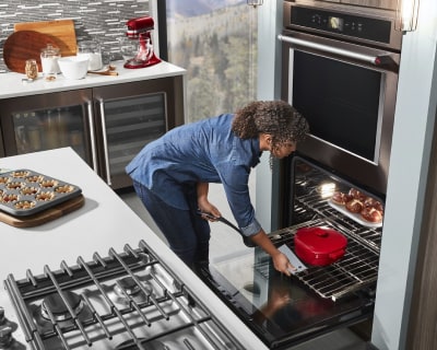 Person removing a dutch oven from a wall oven