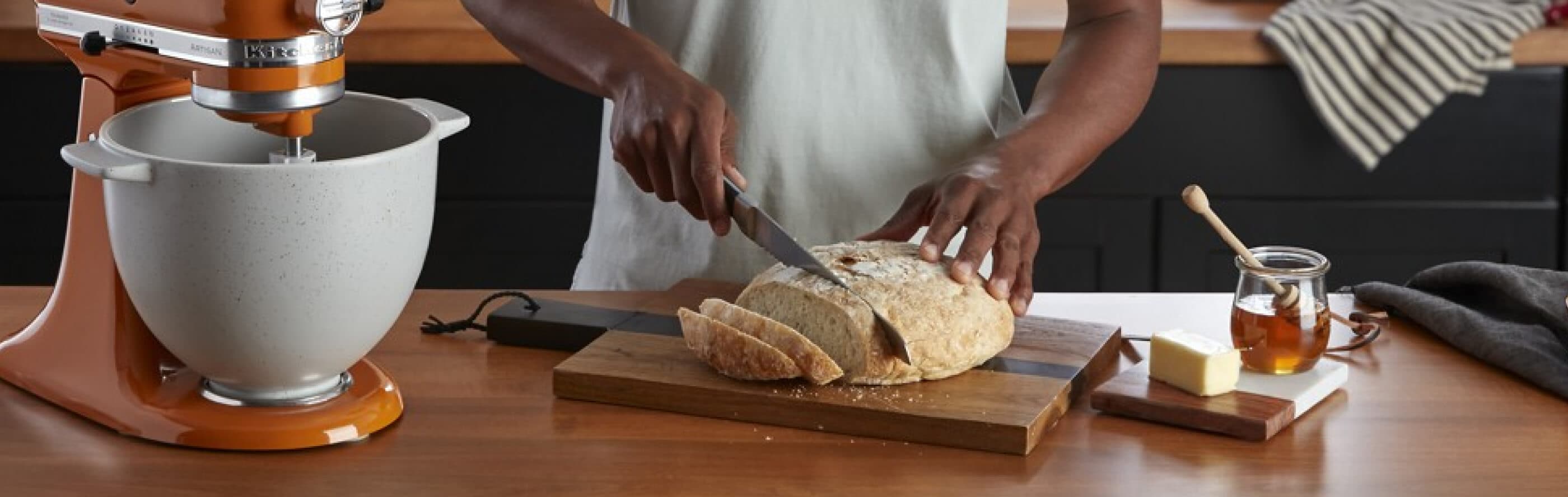 Person slicing a loaf of bread next to a KitchenAid® stand mixer