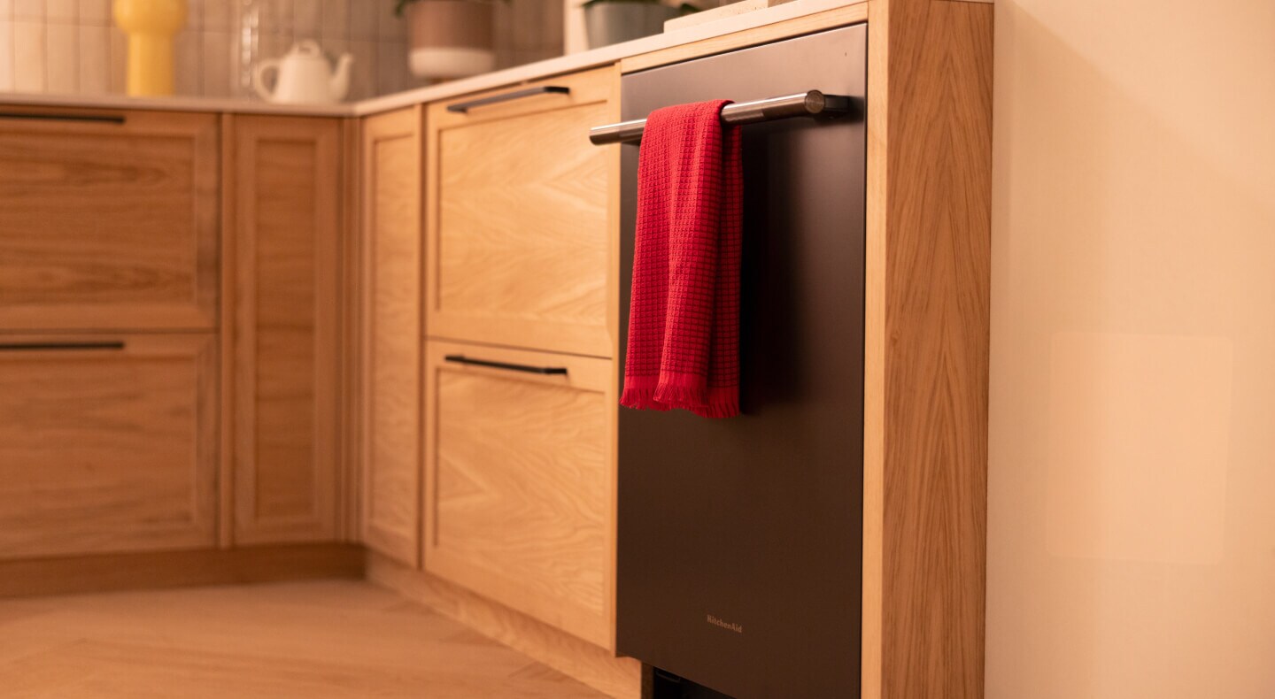 KitchenAid® dishwasher with a bar handle holding a red dish towel
