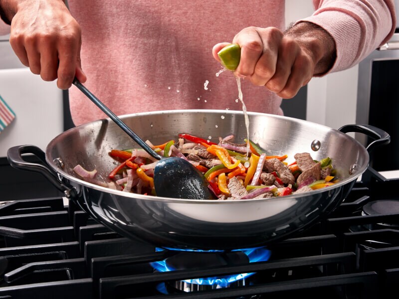 Someone cooking vegetables in a pan on their cooktop