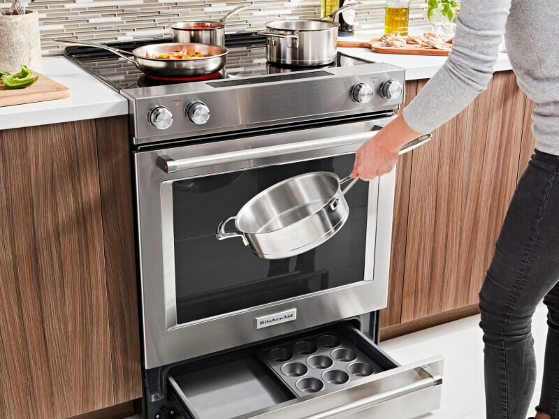 A slide-in range with an open storage drawer showing pans inside