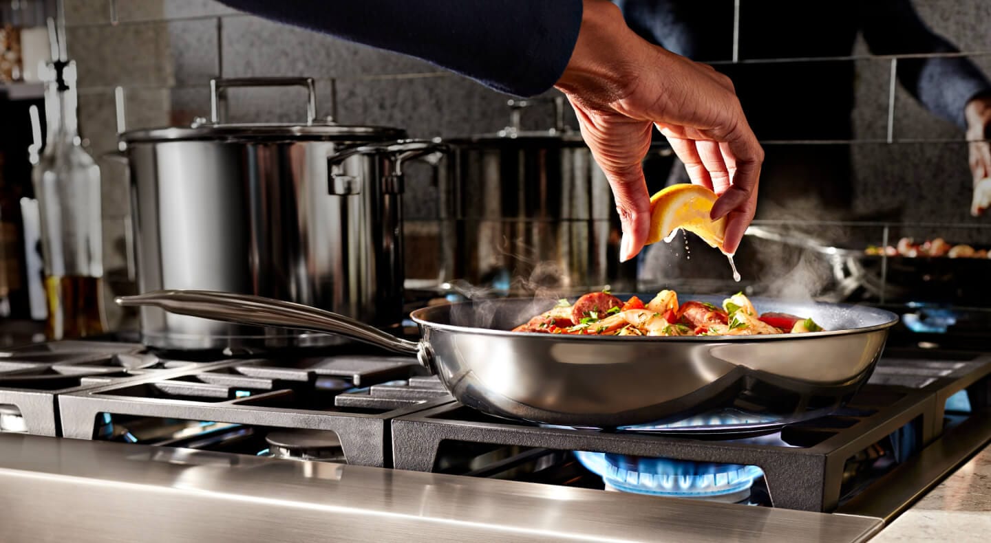A person squeezing a lemon over cooking food on a cookto A person squeezing a lemon over cooking food on a cookto
