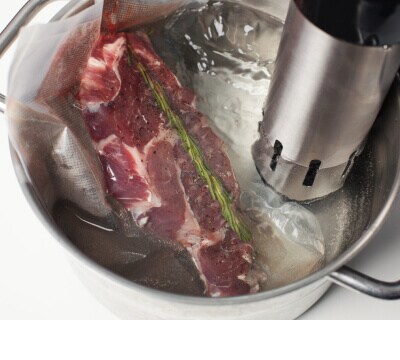Piece of meat seasoned with rosemary in water with circulator tool in it