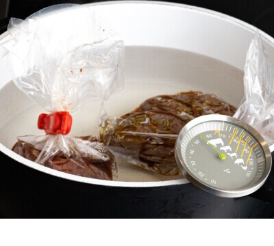 Two pieces of meat in sous vide bags placed inside a pot with a thermometer
