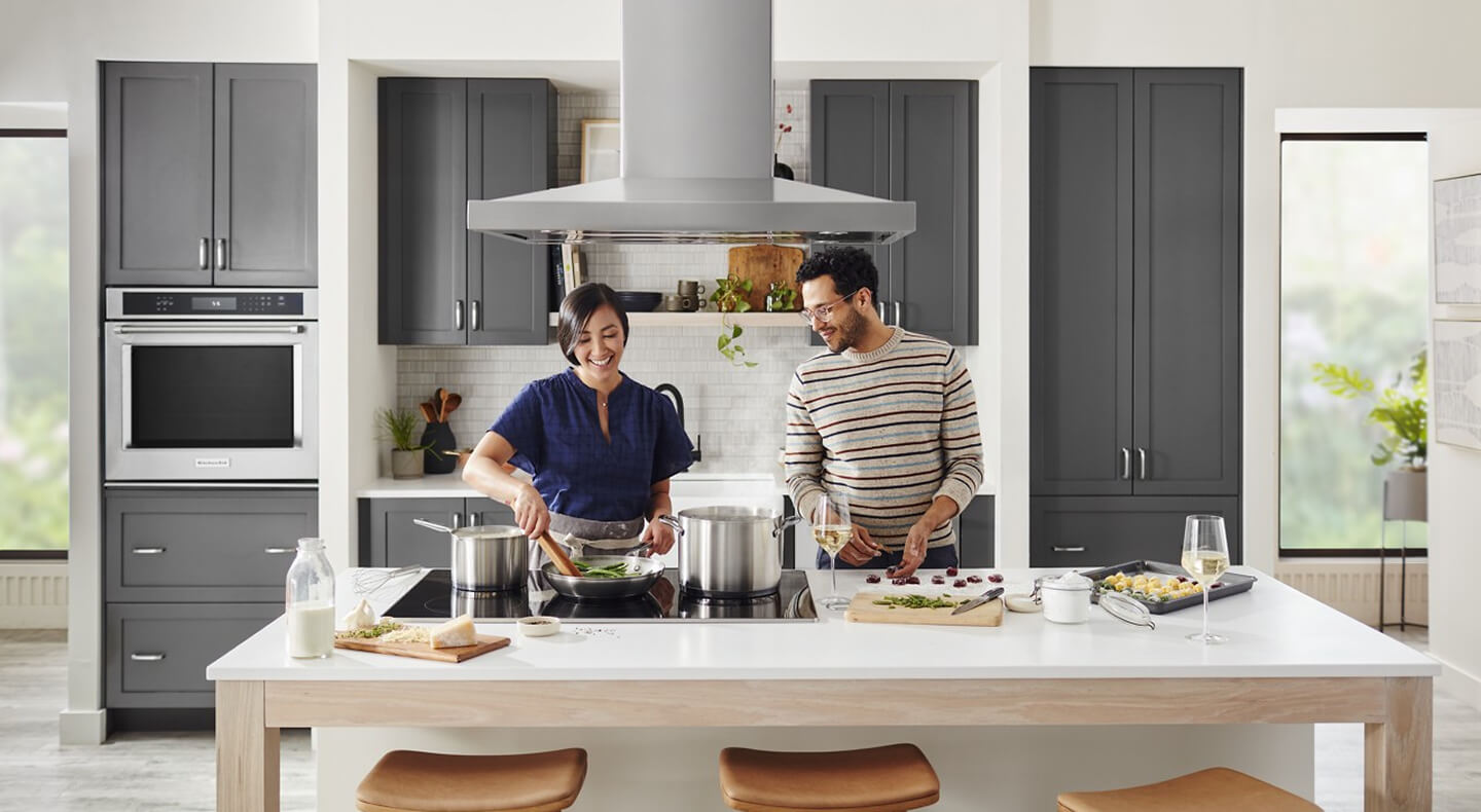 Two people cooking at a kitchen island over a cooktop Two people cooking at a kitchen island over a cooktop